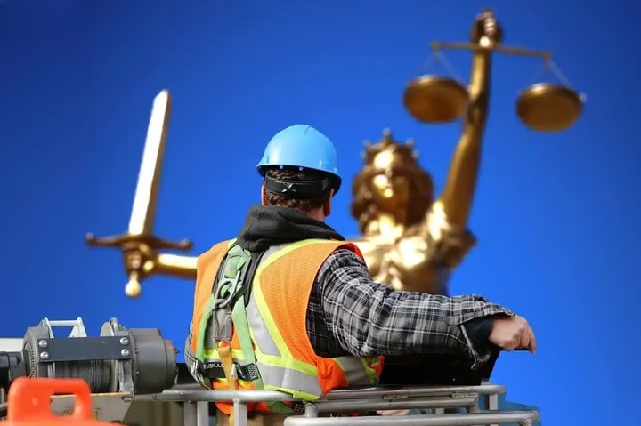 Photo of a man in safety gear facing the statue of a woman carrying a scale and a sword